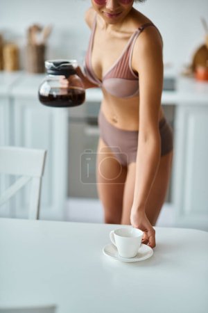 junge afrikanisch-amerikanische Frau mit Augenklappen, die Tasse und Kaffeekanne in der Küche hält