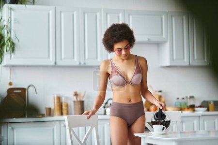 lockige, glückliche afrikanisch-amerikanische Frau mit Augenklappen, die in der Küche Kaffee in Porzellantasse gießt