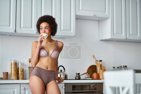 Téléchargez les photos : Femme afro-américaine bouclée avec des patchs debout dans les sous-vêtements et boire du café de tasse - en image libre de droit