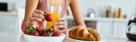 cropped banner of african american woman holding fresh strawberry and orange juice during breakfast