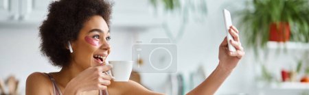 Smiling african american woman in lingerie with eye patches taking selfie with cup of coffee, banner