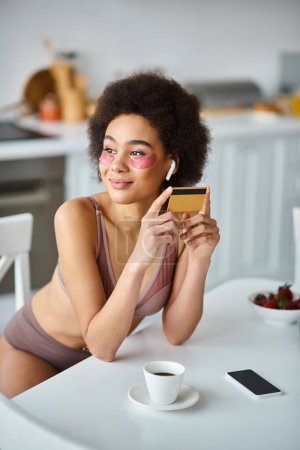 lächelnde Afroamerikanerin mit Kopfhörern mit Pflaster unter den Augen, die mit Kreditkarte einkauft