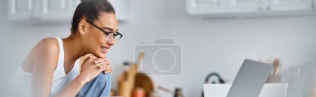 heureuse et jeune femme afro-américaine dans des lunettes de travail de la maison à distance sur son ordinateur portable, bannière