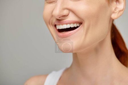 abgeschnittene Ansicht einer glücklichen Frau im Tank-Top, die fröhliches und gesundes Lächeln auf grauem Hintergrund ausstrahlt