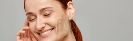 Téléchargez les photos : Femme heureuse et rousse en débardeur blanc avec un sourire tendre et sain sur fond gris, bannière - en image libre de droit