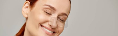 Téléchargez les photos : Femme heureuse et rousse en débardeur blanc souriant avec les yeux fermés sur fond gris, bannière - en image libre de droit
