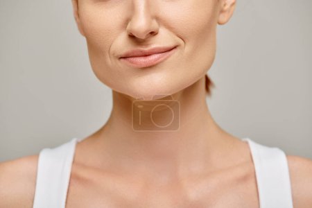 Close-up of a serene woman in her 30s with radiant skin posing on grey background, skin care concept