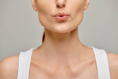 cropped view of woman in her 30s puckering lips on a neutral grey background, blowing Poster #693712342