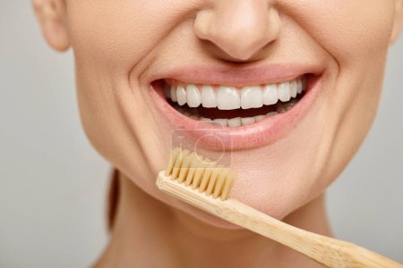 photo recadrée de femme heureuse dans les années 30 avec des dents blanches saines tenant une brosse à dents en bambou, dentaire