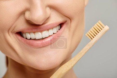 abgeschnittene Aufnahme einer positiven Frau in den 30er Jahren mit weißen gesunden Zähnen, die eine Bambuszahnbürste in der Hand hält, Nahaufnahme