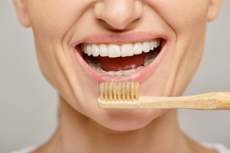 Schnappschuss einer glücklichen Frau in den 30er Jahren mit weißen gesunden Zähnen, die eine Bambuszahnbürste hält, offenen Mund