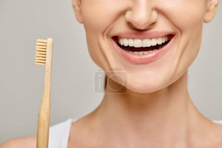 cropped photo of joyous woman in 30s with white healthy teeth holding a bamboo toothbrush