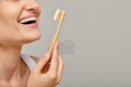 Photo for Cropped shot of joyful woman holding toothbrush with toothpaste and smiling on grey backdrop - Royalty Free Image
