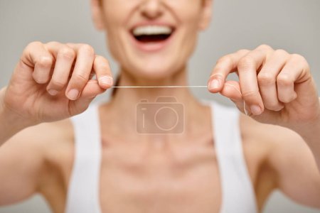 enfoque en hilo dental sobre fondo gris, vista recortada de la mujer feliz que promueve la higiene bucal