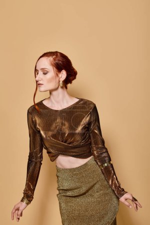 redhead model in her 30s posing in glamorous attire and golden accessories on beige backdrop