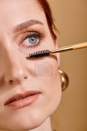 close up photo of redhead woman with green eyes applying mascara on beige background, makeup