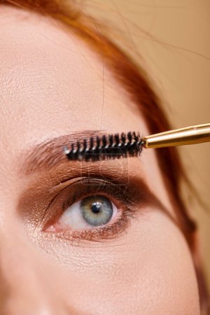 abgeschnittene Ansicht einer Frau mit grünen Augen, die Mascara auf beigem Hintergrund aufträgt, Make-up und Schönheit
