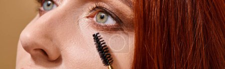 Photo for Cropped banner of woman with green eyes applying mascara on beige background, makeup routine - Royalty Free Image