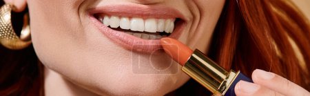 cropped banner of woman smiling and applying nude lipstick on beige background, white teeth