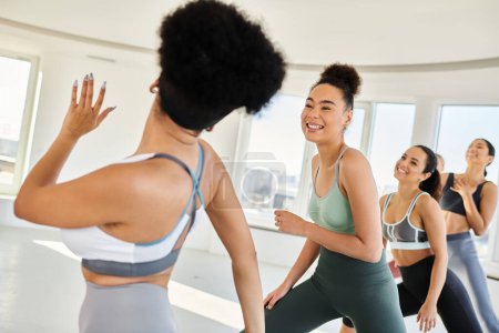 Photo for Group of young diverse women in sportswear practicing pilates with female trainer, wave hand - Royalty Free Image
