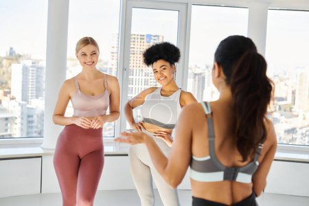 Pilates Trainerin im Gespräch mit fröhlichen multiethnischen Frau in Sportbekleidung vor dem Unterricht, Sport