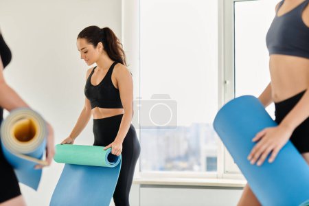 young and brunette woman in her 20s standing with fitness mat and standing near female friends