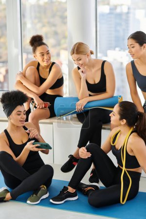 happy african american woman showing smartphone to her friends after workout in pilates studio