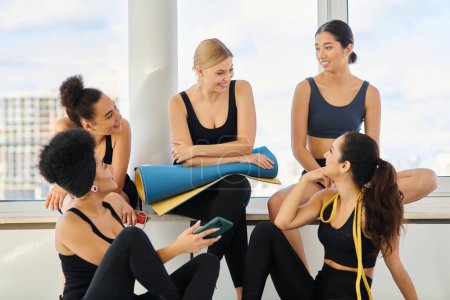 african american woman showing smartphone to her happy friends after workout in pilates studio