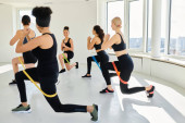 group of diverse women in sportswear looking at happy trainer and doing lunges with resistance bands Stickers #693842556