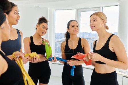 Photo for Group of young diverse sportswomen holding resistance bands and chatting after pilates workout - Royalty Free Image