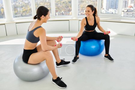 fröhliche Freundinnen beim Training mit Kurzhanteln auf Fitnessbällen im Pilates-Kurs