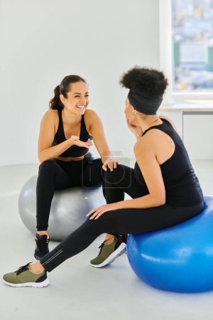Photo for Happy and diverse female friends sitting on fitness balls and chatting before pilates workout - Royalty Free Image