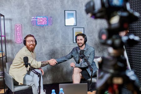 gutaussehender Interviewer und sein Gast in lässiger Kleidung schütteln Hände und lächeln glücklich, Podcast