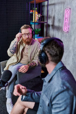 Photo for Handsome interviewer with red hair and his guest with headphones discussing questions, podcast - Royalty Free Image