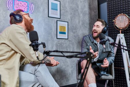 attraktiver Interviewer mit roten Haaren und sein Gast mit Kopfhörern, der Fragen diskutiert, Podcast