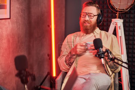 fröhlicher gutaussehender Mann mit rotem Bart und Kopfhörer in lässiger Kleidung, der während eines Podcasts plaudert