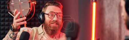 cheerful handsome man with red beard with headphones in casual clothes talking during podcast