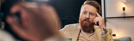 hombre barbudo de buen aspecto con el pelo rojo en ropa elegante sentado junto a su entrevistador, pancarta