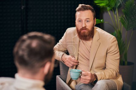 hombre de pelo rojo bien parecido con taza de café sentado durante la discusión junto a su entrevistador