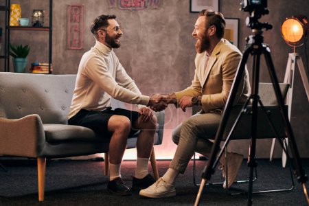 Photo for Handsome interviewer and his guest in casual attires shaking hands and smiling happily, podcast - Royalty Free Image