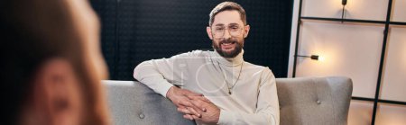 Photo for Cheerful bearded men in casual outfit smiling and looking at his interviewer while in studio, banner - Royalty Free Image