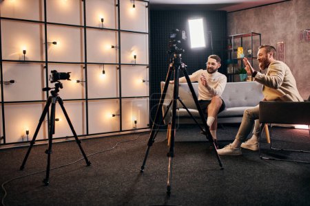 beaux hommes élégants avec barbe en tenue chic agitant à la caméra lors d'une interview en studio