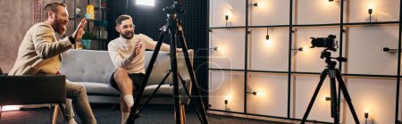 gutaussehende elegante Männer mit Bärten in schicken Anzügen winken während des Interviews im Studio in die Kamera, Banner