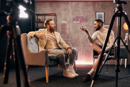two elegant men with beards with dapper style sitting and discussing interview questions in studio