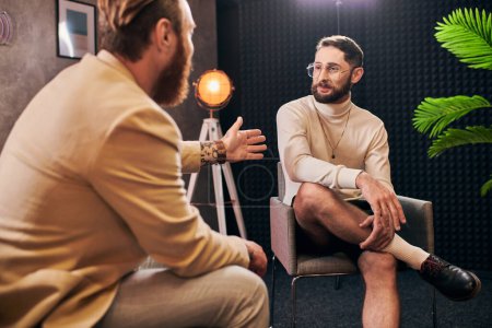 attractive elegant men in stylish clothes sitting and discussing interview questions in studio