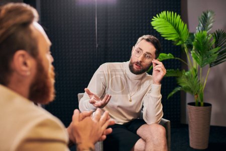 hommes élégants dédiés en vêtements debonair assis et discuter des questions d'entrevue en studio