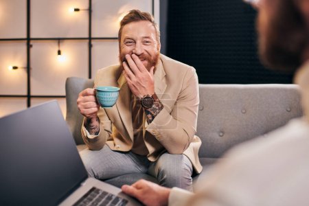 Foto de Dos hombres atractivos alegres en trajes elegantes con café y computadora portátil discutir preguntas de la entrevista - Imagen libre de derechos