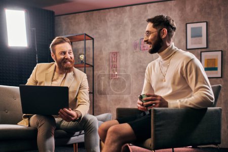 Foto de Dos alegres hombres atractivos en trajes elegantes con café y portátil discutir preguntas de la entrevista - Imagen libre de derechos