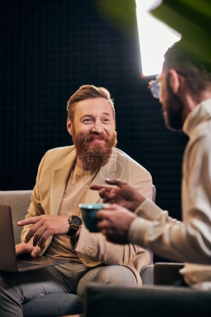 Foto de Dos hombres guapos alegres en trajes elegantes con café y computadora portátil discutir preguntas de la entrevista - Imagen libre de derechos