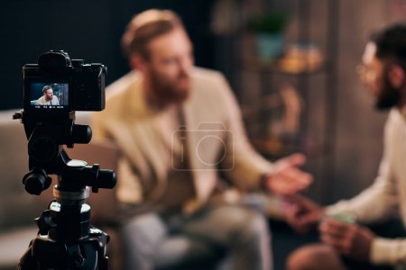Foto de Enfoque en la cámara de filmación elegante hombres borrosos con barbas en trajes elegantes discutir preguntas - Imagen libre de derechos